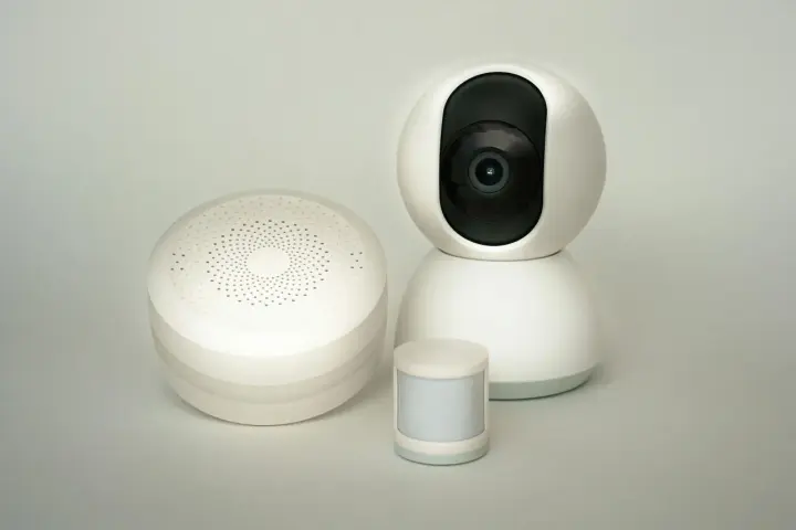 Trzy białe urządzenia smart home: okrągły głośnik, kamera IP i mały czujnik ruchu. Różne rodzaje czujników ruchu.